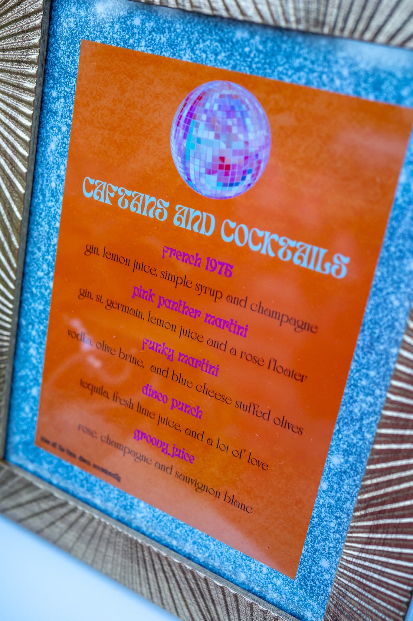 Caftans and Cocktails retro-style cocktail menu in a gold frame